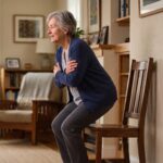 Older adult rising from a chair with arms crossed